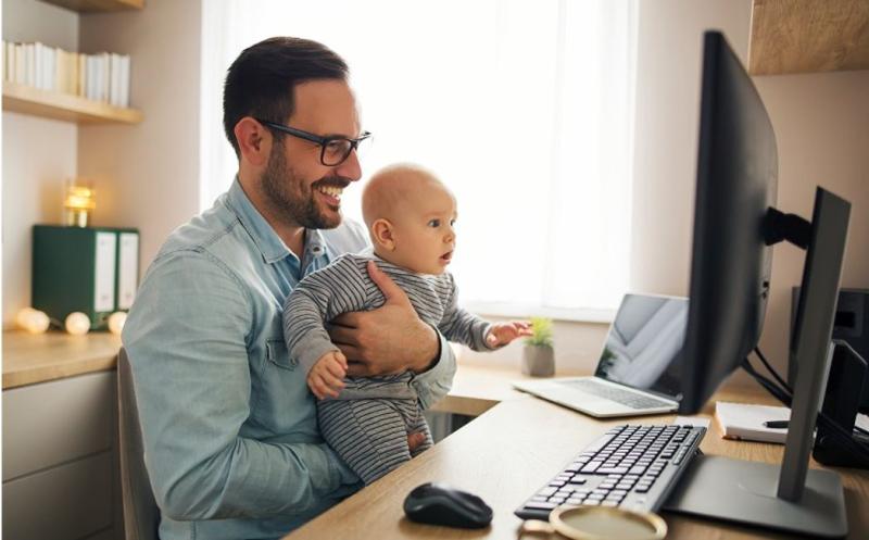 dad holding a baby while working from home on desk
